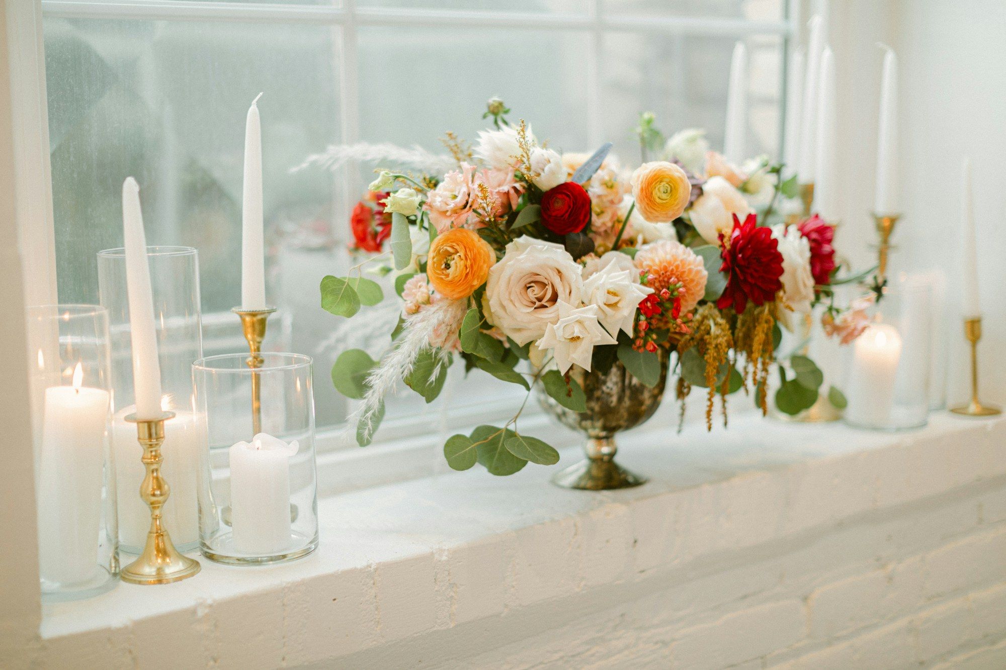A low floral arrangement in a gold compote beside candles