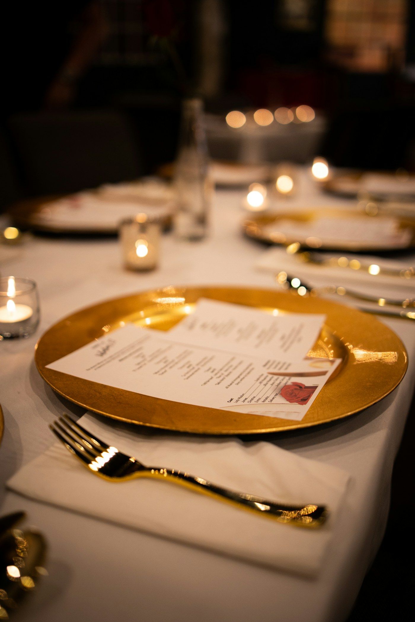 A gold charger plate holding a printed menu on a candlelit table