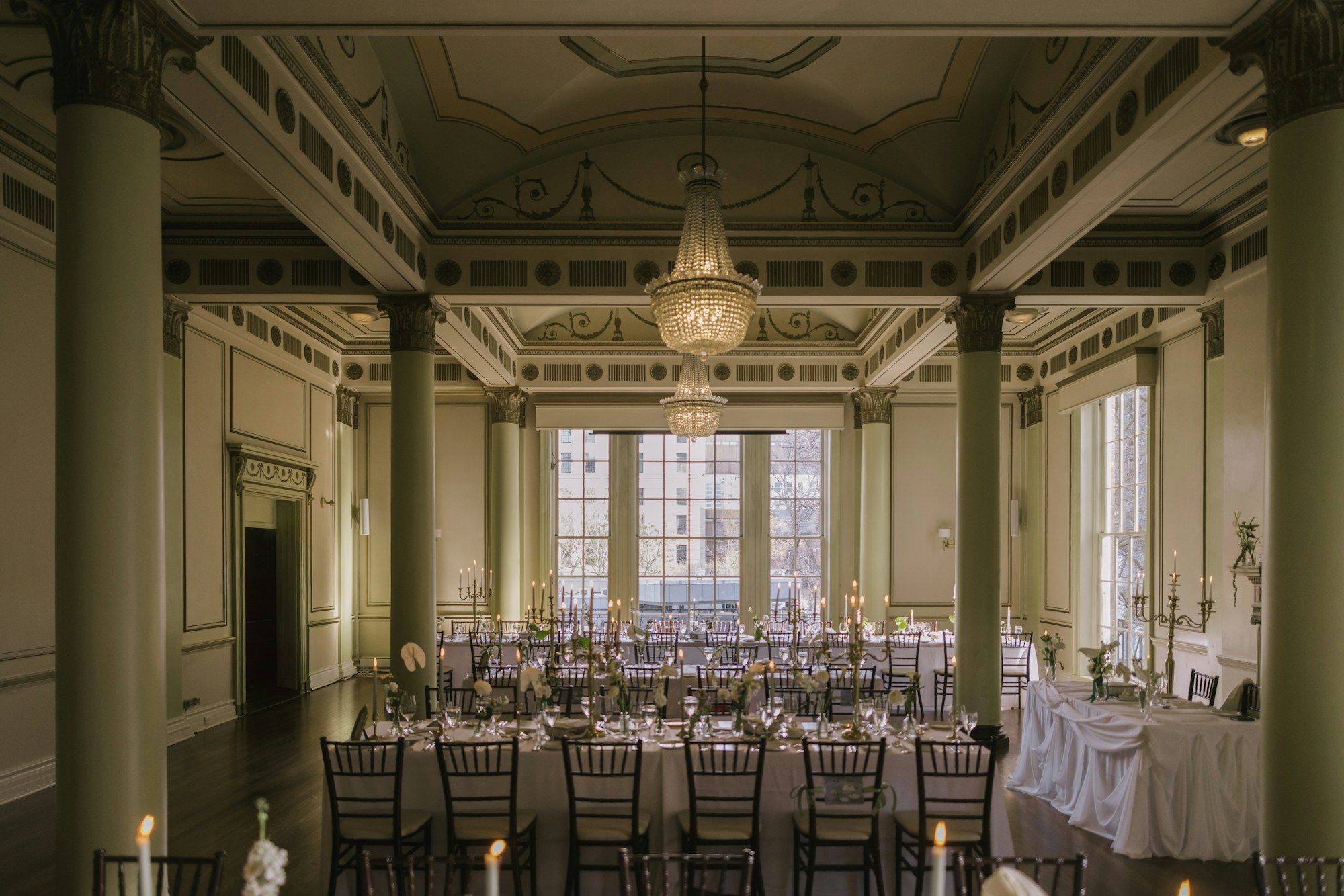 A grand ballroom with columns and chandeliers, laid for dinner