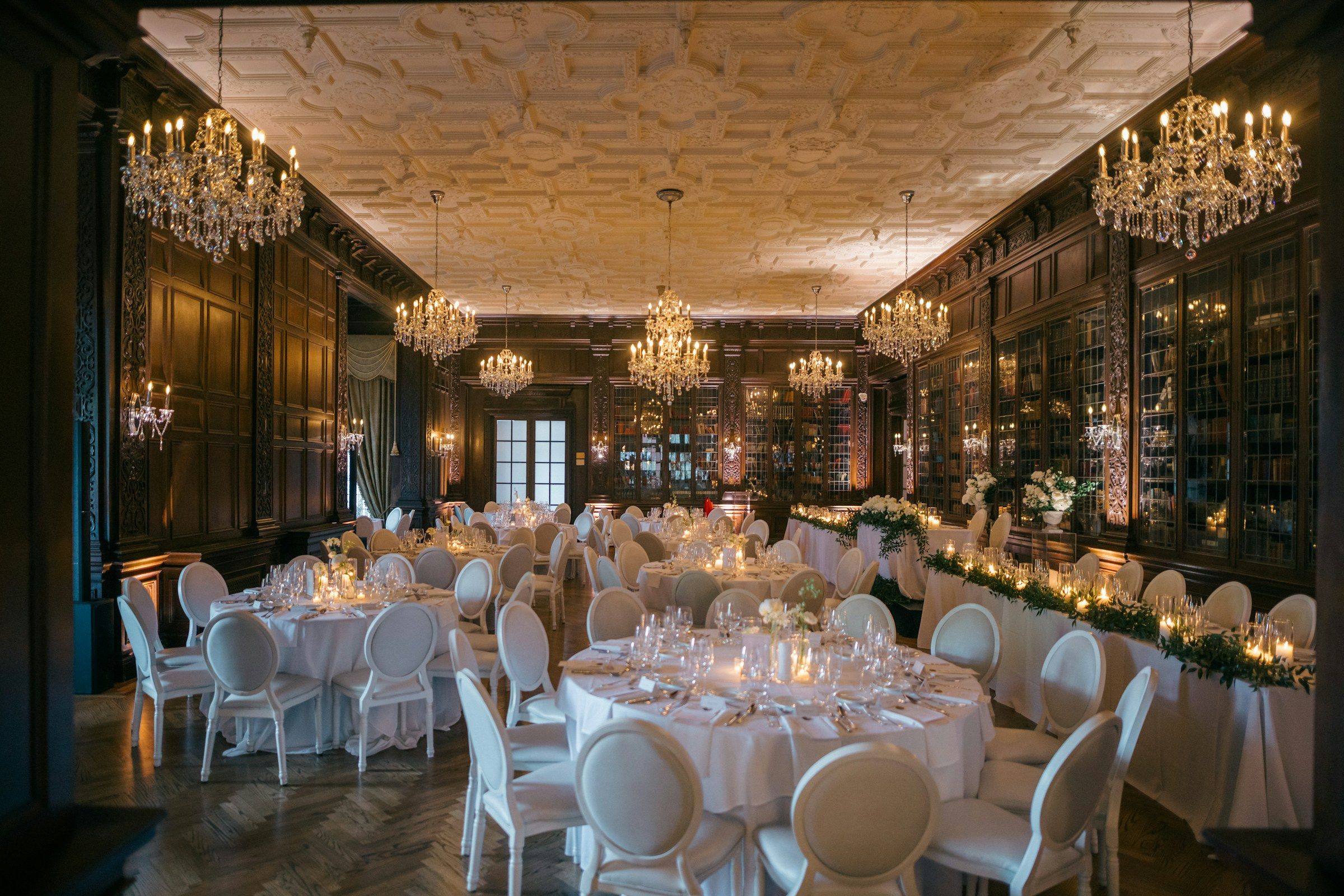 A panelled dining room set for a formal dinner beneath crystal chandeliers